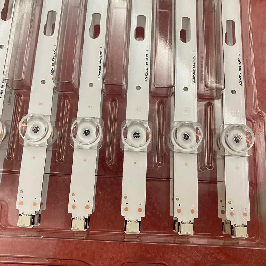 Close-up of LED backlight strip components with lenses, mounted on circuit boards in plastic packaging.