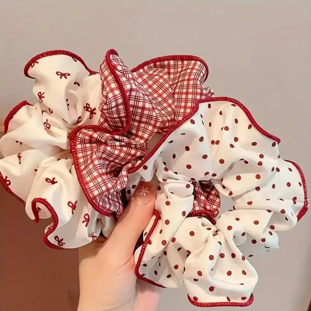 A set of red and white hair scrunchies with polka dot and plaid patterns being held in a hand