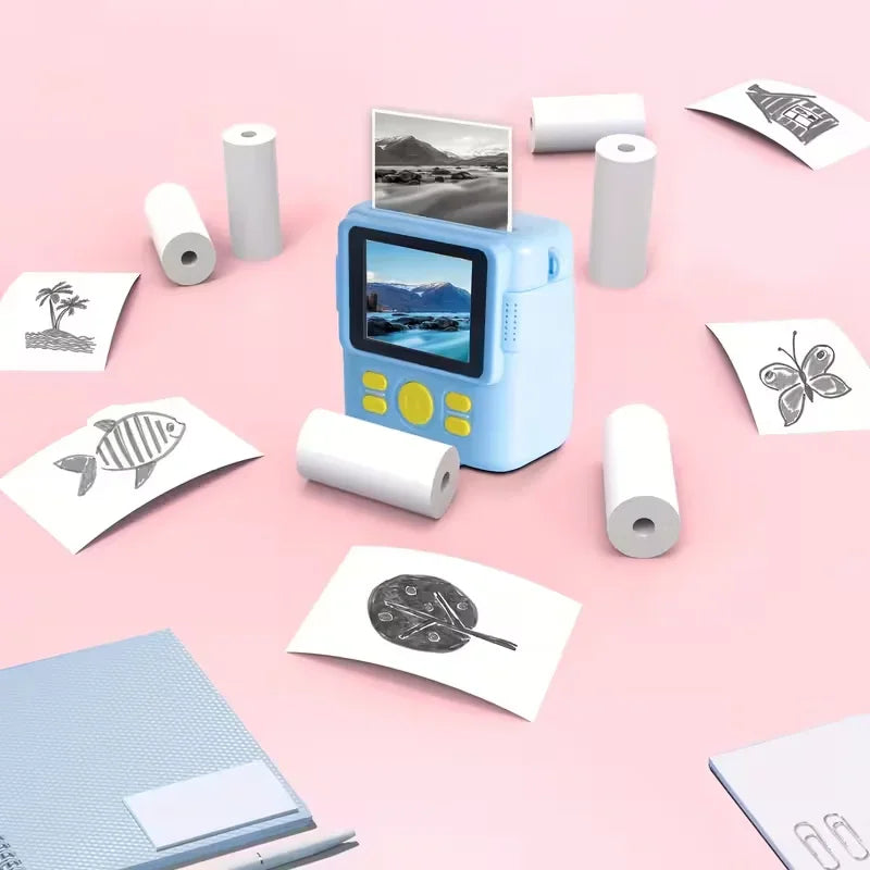 Light blue instant camera with thermal paper rolls and printed black and white drawings on a pink surface