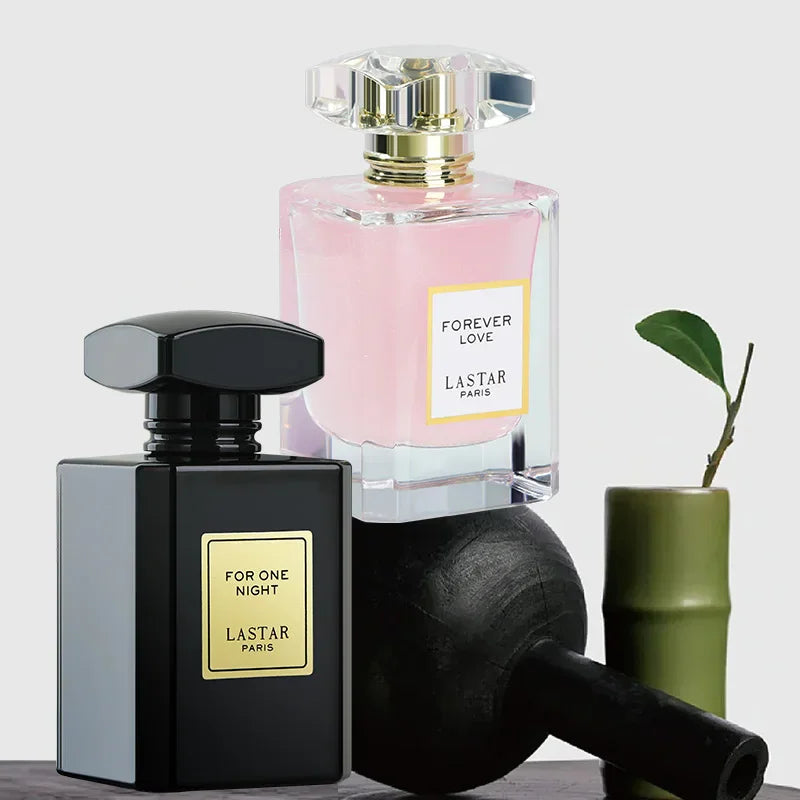 A pink perfume bottle and a black perfume bottle displayed with decorative black and green objects.