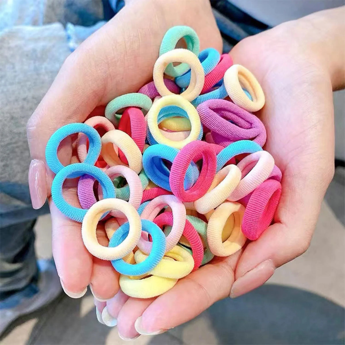 Hands holding a collection of assorted small pastel seamless fabric hair elastics