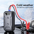 Portable car jump starter with jumper cables connected to a battery in a snowy environment