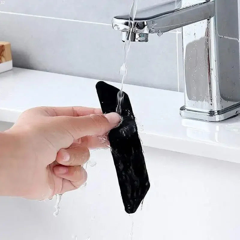 A hand washing a black adhesive rug gripper under a water faucet