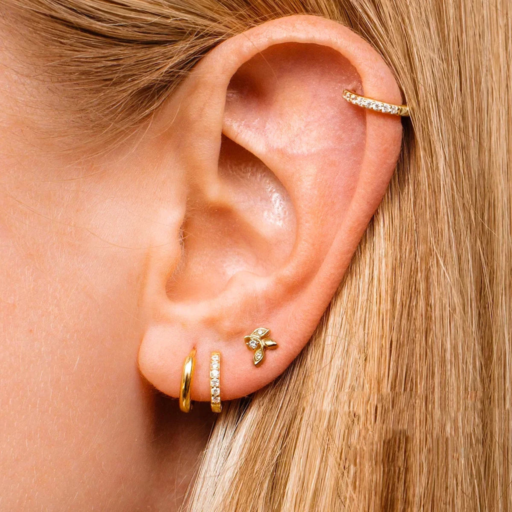 Gold hoop earring with crystals worn as a cartilage piercing in an ear with blonde hair.