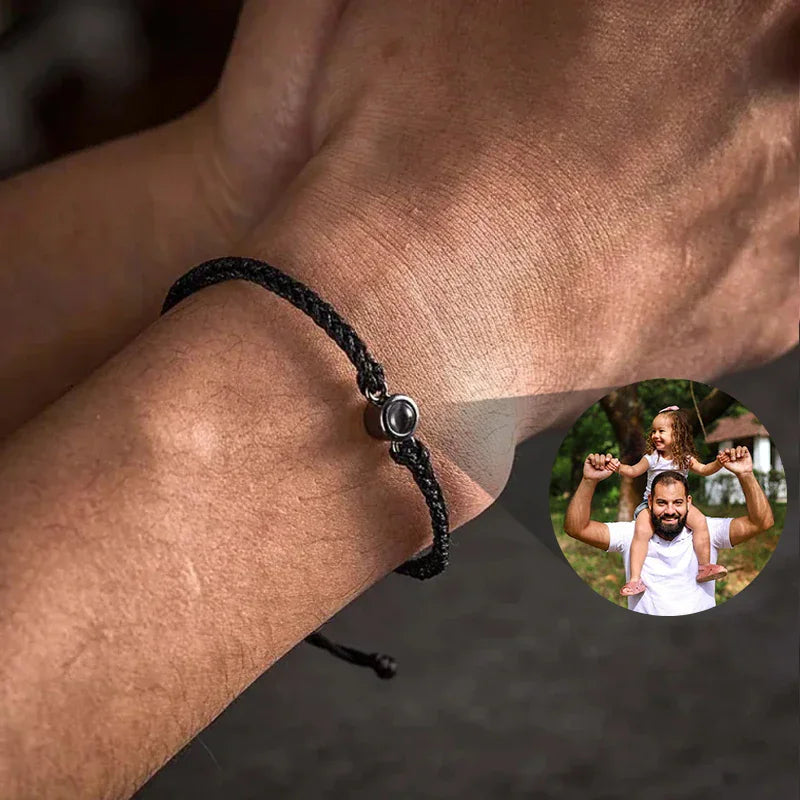 A black woven rope bracelet with a circular center charm that projects a photo of a father and child.