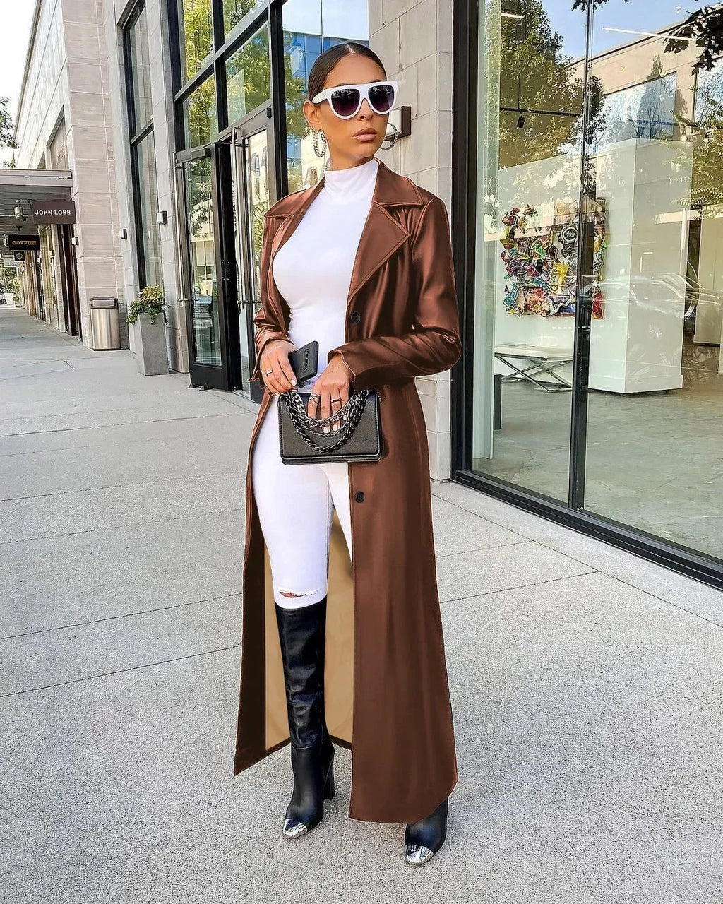 A woman wearing a brown leather trench coat over a white top and pants.