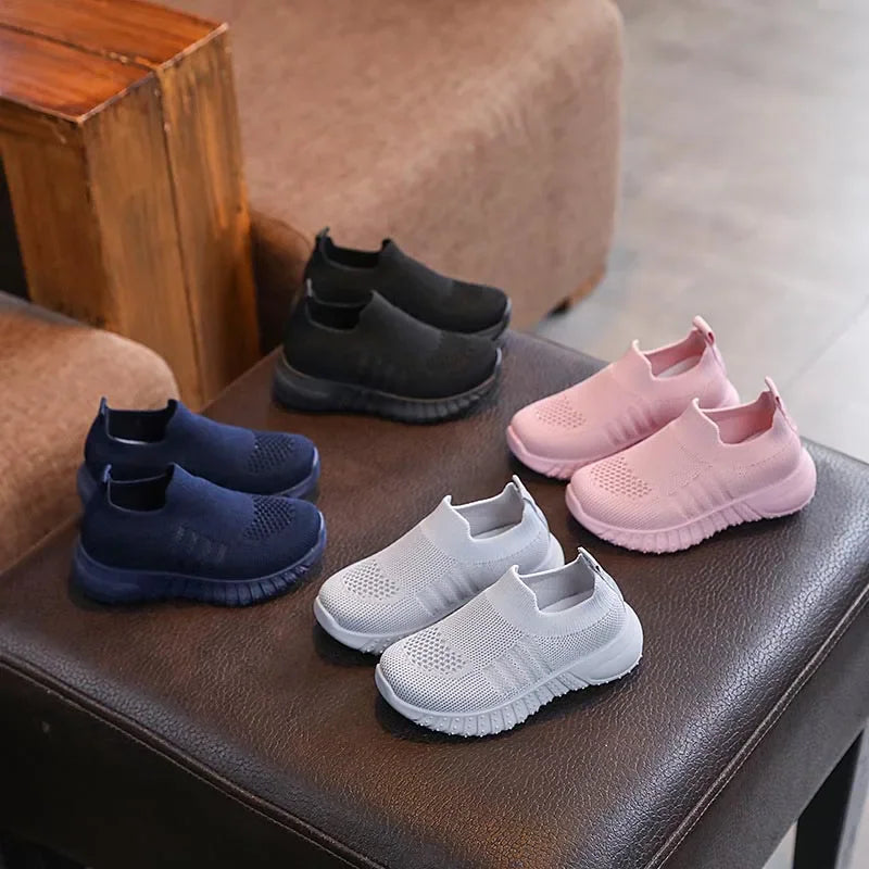 A collection of children's slip-on knitted sneakers in black, navy blue, pink, and light grey