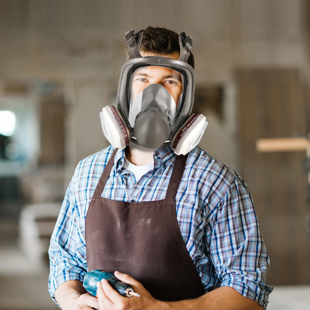 Man in a workshop wearing a full face respirator mask for protection while working with a drill