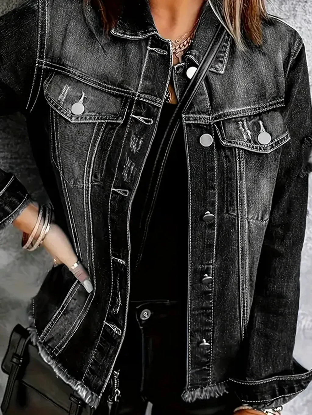 Close-up of a person wearing a dark grey distressed button-up denim jacket and gold jewelry