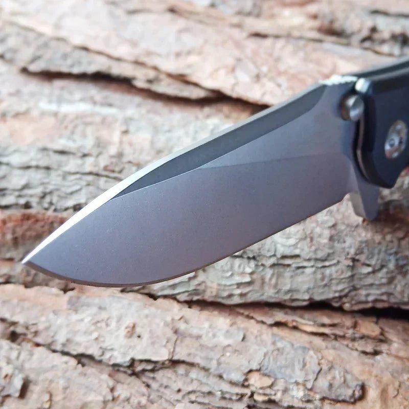 Close-up detail of a folding pocket knife blade with a metallic finish on a wood bark surface