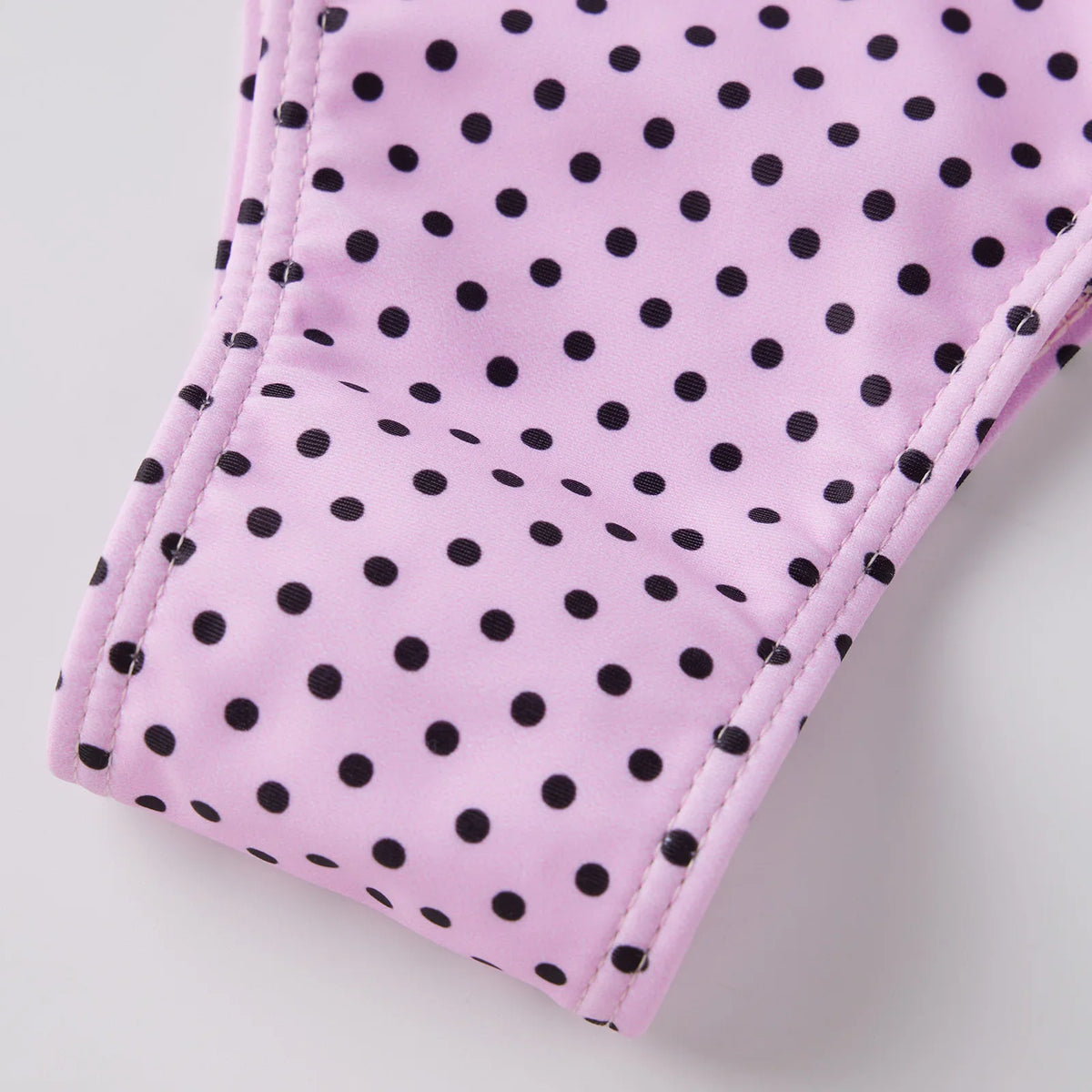 Close-up of the fabric and ruffle detail of a pink and black polka dot bikini bottom.
