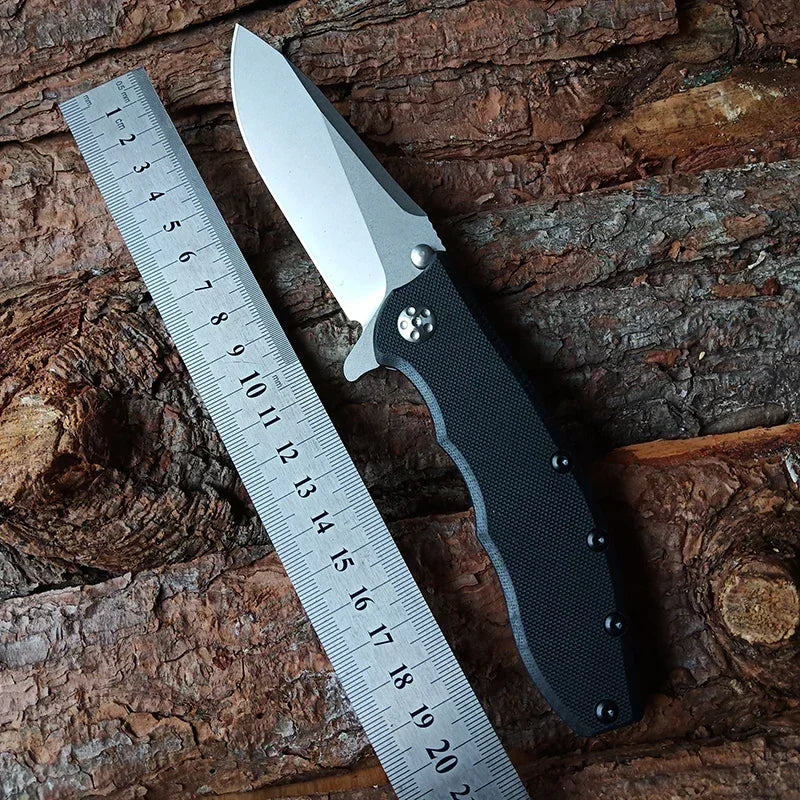 Folding pocket knife with a black handle and steel blade resting next to a metal ruler on a wooden surface