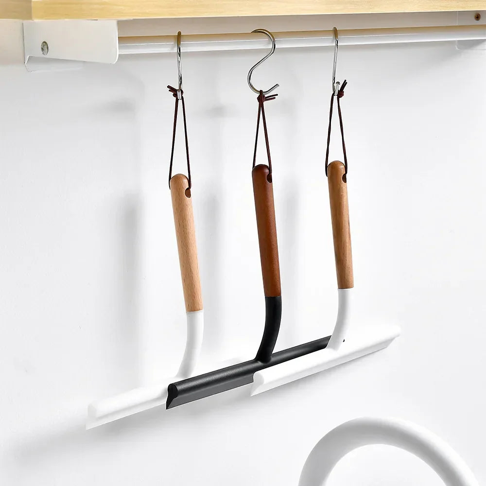 Three silicone window wipers with wooden handles hanging from hooks on a shelf