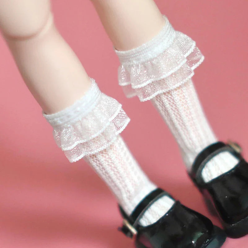 Close up of white lace trim knee-high socks for dolls worn with black Mary Jane shoes