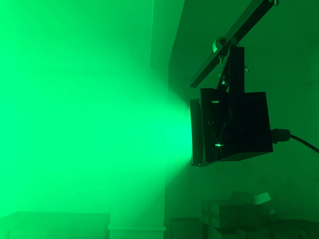 Black stage blinder light emitting a bright green wash beam in a dark room