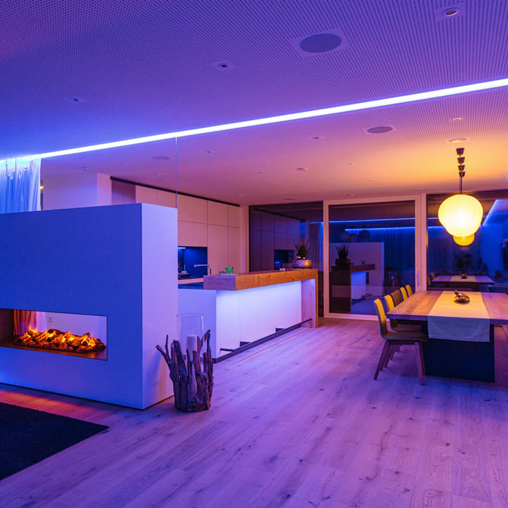 A contemporary open-plan dining and living area lit by purple and warm-toned ceiling-mounted LED strips.