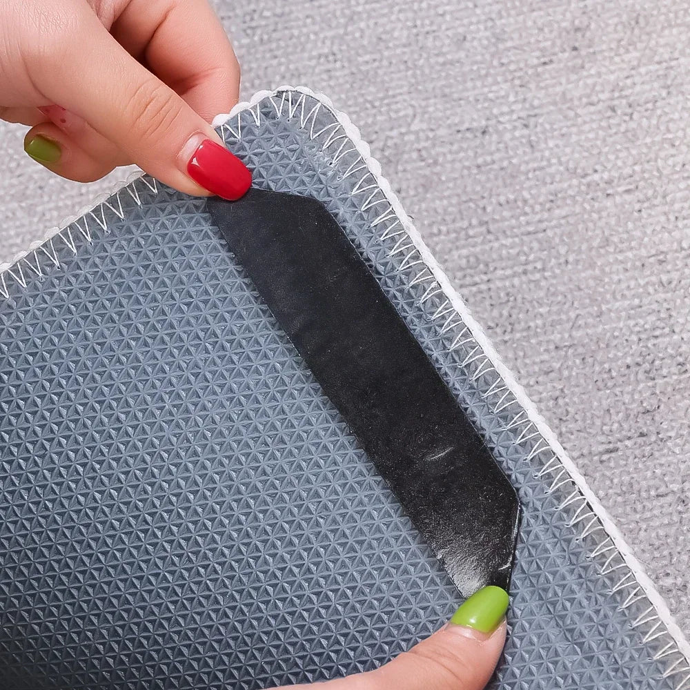 Hands pressing a black rug gripper onto the corner of a grey anti-slip rug